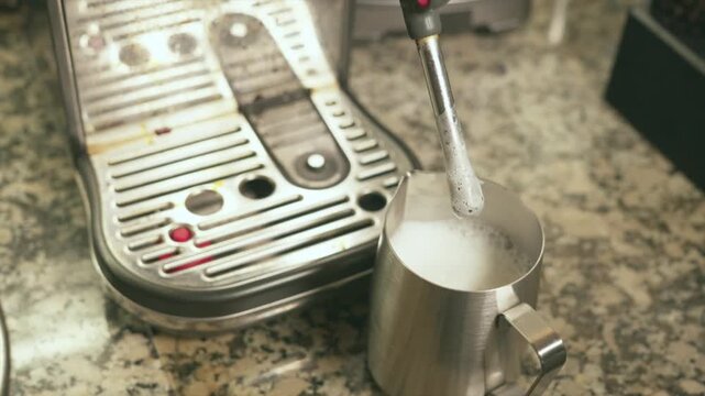 Professional barista steaming milk with a coffee machine wand
