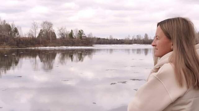 Woman standing near spring lake with ice on lake calm reflection by lake in changing season Peaceful spring mood soft light mindful moment nature transition from winter to spring serene atmosphere