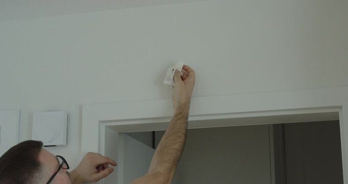 Man removing a small insect from a wall inside a home using a tissue.