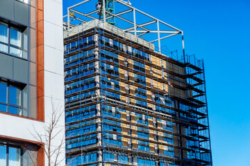 High-rise under construction with scaffolding. Blue sky contrasts with steel and glass. Building reflects sunlight in its windows. Worker's silhouette seen near crane © Алексей Петров
