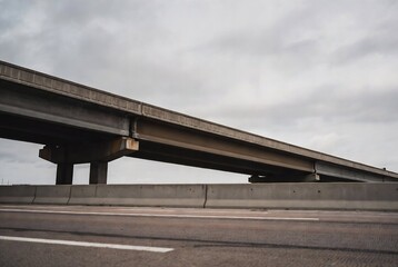 Fototapeta premium A concrete overpass spans a highway under a cloudy sky.