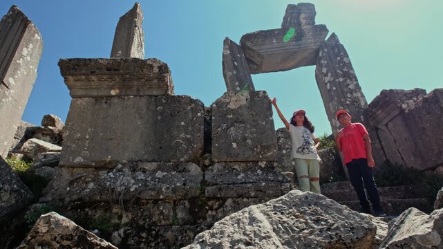 Two young people exploring ancient stone gateway ruins at Termessos Ancient City in Antalya, Turkey. A scenic blend of history, nature and travel, highlighting cultural heritage and discovery.