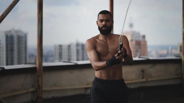 Man with muscular physique jumping with rope on empty rooftop, cardio training