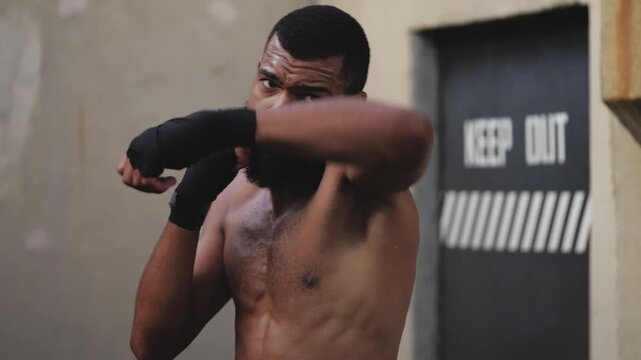 Young Black male fighter with muscular body practicing shadow boxing, workout