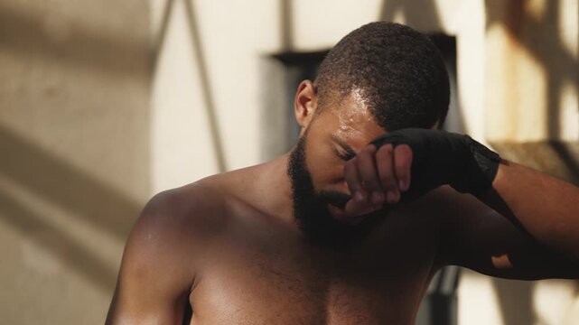 Tired African American man fighter wiping sweat after active boxing training