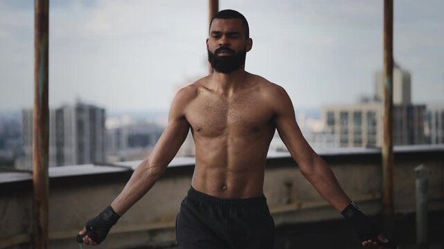 Young Black male with athletic build exercising with jump rope on empty rooftop