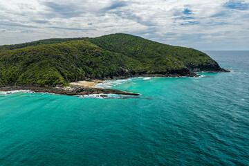 Naklejka premium Aerial view of Sharkies Beach with tree covered mountain and rocky coastline