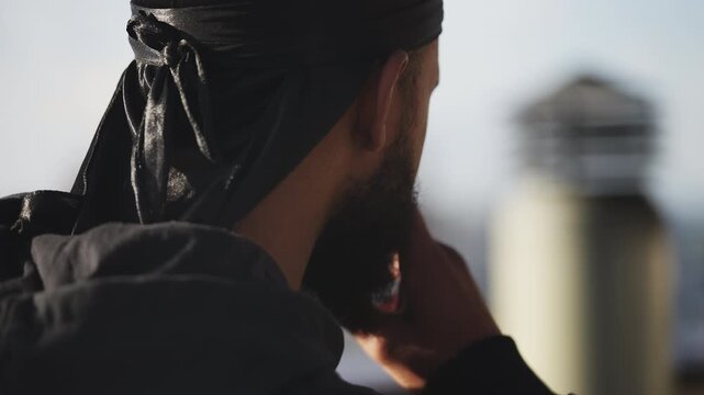 Confident Black man in a durag smoking cigarette on rooftop, rebellious vibe