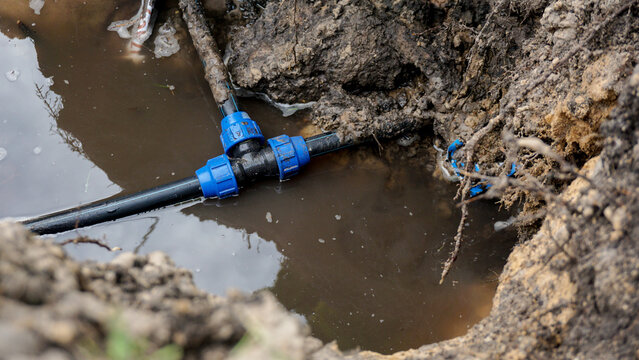 Underground water pipe with blue plastic compression fittings submerged in muddy flooded excavation pit, water leak repair, plumbing emergency, or utility infrastructure maintenance