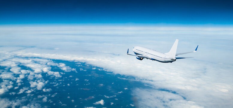 Airplane flying in the sky over the land surface, white commercial airplane in the flight in the stratosphere