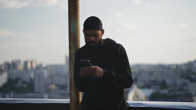 Young African American man in a hoodie checking phone messages on rooftop