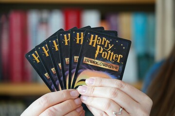 Naklejka premium WARSAW, POLAND - MARCH 19, 2026: Person holding a hand of Harry Potter Trading Card Game, a collectible card game based in the world of Harry Potter novels. It was published by Wizards of the Coast.