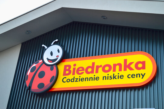 Modern Biedronka supermarket storefront sign featuring the iconic ladybug logo on a dark gray corrugated wall in Poland under bright natural daylight conditions.
