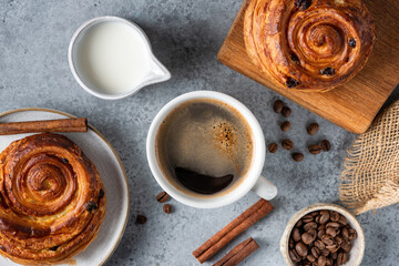 Table top view of breakfast in cafe: cup of black coffee, milk in jug, sweet cinnamon raisin buns
