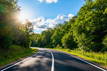 Obraz premium Winding Road Through Lush Green Forest Under Blue Sky