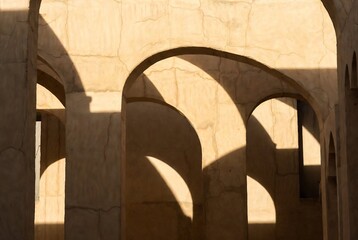 Naklejka premium Arched columns cast shadows on a textured wall within an ancient structure.