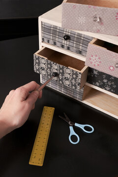 Hand pointing with a pencil into a decorative wooden drawer unit