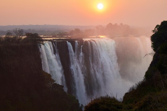 Spectacular sunrise over Victoria Falls (Mosi-oa-Tunya) with mist and golden sunlight, Zambezi River, border of Zambia and Zimbabwe. Majestic African landscape and natural wonder 
