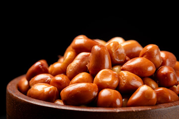 Obraz premium Close-up of crispy brown fried peanuts in wooden bowl on a black background.