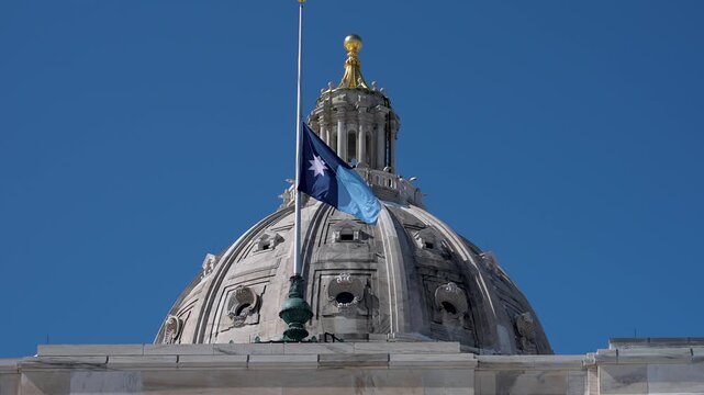 A Minnesota state flag flies in the wind at the top of the State Capitol building in Saint Paul on a sunny day.