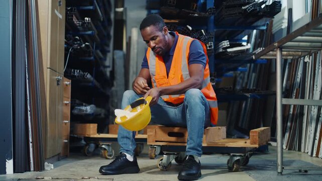 African American worker feeling overwhelmed and tired, taking a break from extreme job stress and burnout in an industrial storage warehouse.