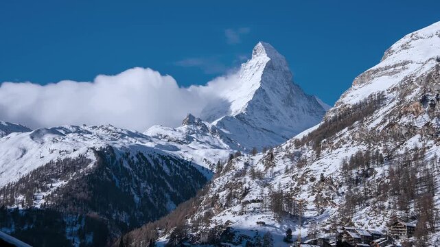 Timelapse panorama shows the Matterhorn above Zermatt in the Swiss Alps. Clouds stream and wrap around the peak as light shifts over bright snow and rock.