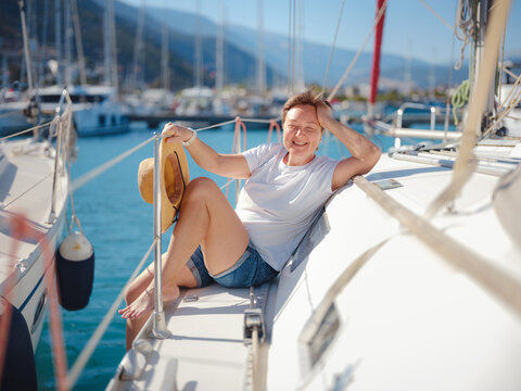 Mature woman relaxes on private yacht during sunny day in Finike Marina. Turkish coastline and luxury boats surround sailing vessel in Mediterranean port during summer vacation.