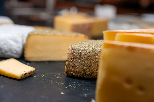 Assorted artisanal cheeses sit on a dark slate counter in Zermatt, Switzerland. Semi hard wheels, a herb crusted round, and sliced pieces show smooth interiors.