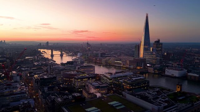 Establishing aerial view of the skyline of London, UK, during a golden sunrise with London and Tower Bridge, City skycrapers and river Thames