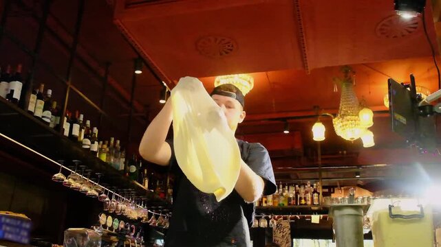Pizzaiolo maintains consistent rotation to achieve uniform base. Pizza base becomes uniformly thin from center to edge. Slow motion
