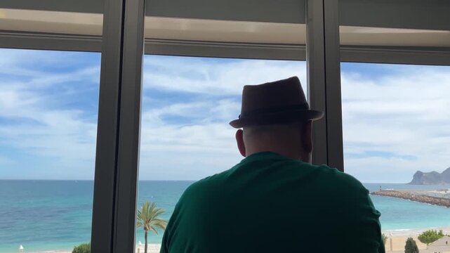 Hombre cerrando ventana y contemplando el mar