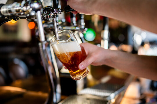 Close-up of a bartender pouring a fresh amber beer from a chrome tap into a glass with foam in a bar.