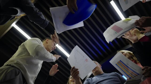 A diverse business team celebrates success, throwing documents and papers excitedly into the air. Colleagues express joy and achievement as reports fly upwards.