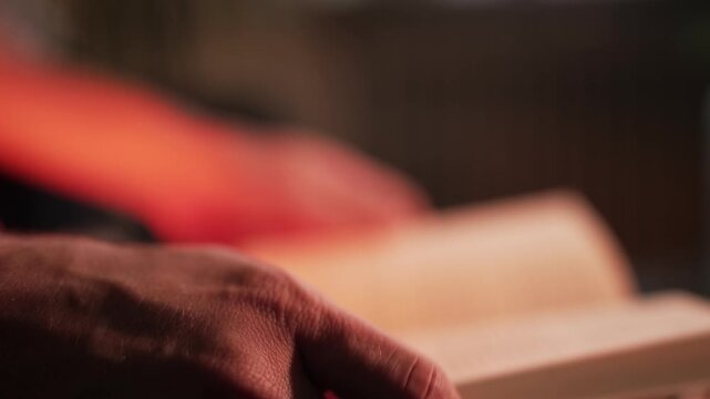 Close-up of a person flipping pages of an old book, hand reading in soft warm lighting, education and library concept, cinematic 4k footage.
