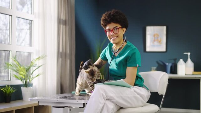 A woman examines a cat in a vet office. She uses tools to check the cat's health. The room has plants and medical supplies. The visit is part of regular care for pets.