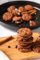 Fototapeta premium A stack of delicious chocolate cookies on a wooden cutting board with cookie crumbs on a plate isolated on a white background.