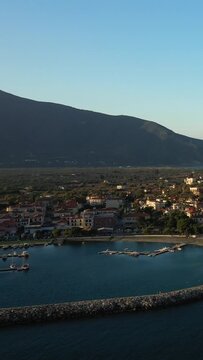 Aerial view of the marina and waterfront buildings in Paralio Astros, Greece, with mountains in the background under a clear sky.