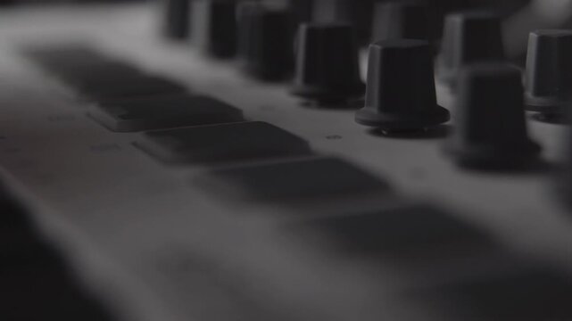 Close up of hands pressing illuminated buttons on a music production device in dim light