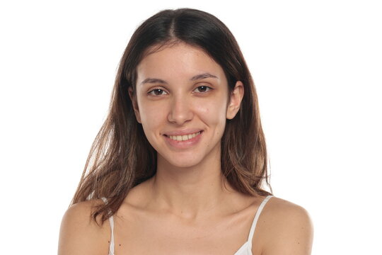 Studio shot of a young brunette woman in white top with no makeup, smiling, portrait, natural look on white background