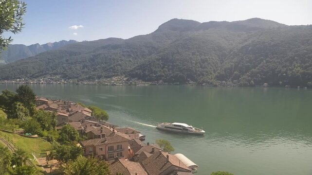 Panoramic elevated view of lake Lugano and Morcote village on a sunny summer day with tourist boat departing
