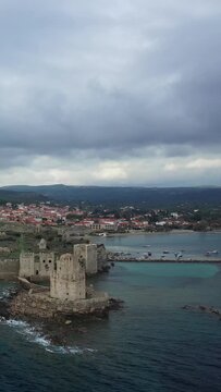 Aerial view of Methoni Castle by the sea with a coastal village and dramatic cloudy sky in the background, located in Methoni, Greece.