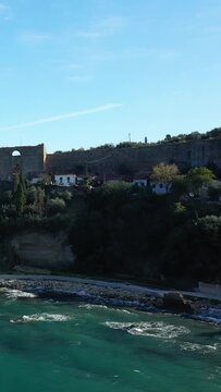 Scenic coastal landscape featuring turquoise waters, rocky shoreline, and historic stone fortress walls in Koroni, Greece. Lush greenery and traditional houses complete the tranquil Mediterranean