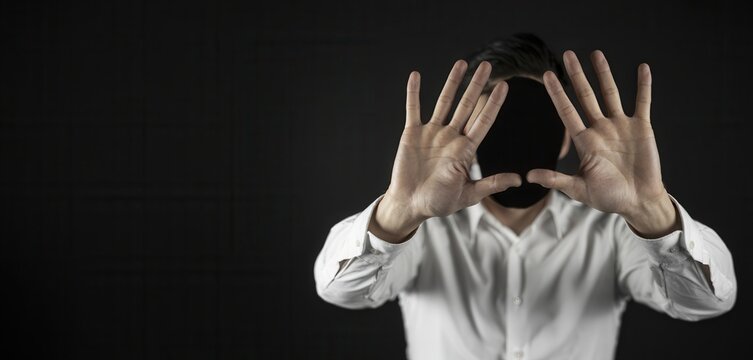 Man covering face with hands in a white shirt on dark background