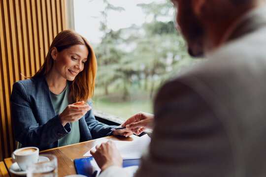 Businessman giving a pen to his colleague to sign a document in a cafe