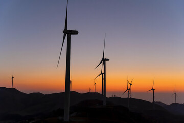 Obraz premium Wind Turbines Silhouetted Against Golden Sunset Sky