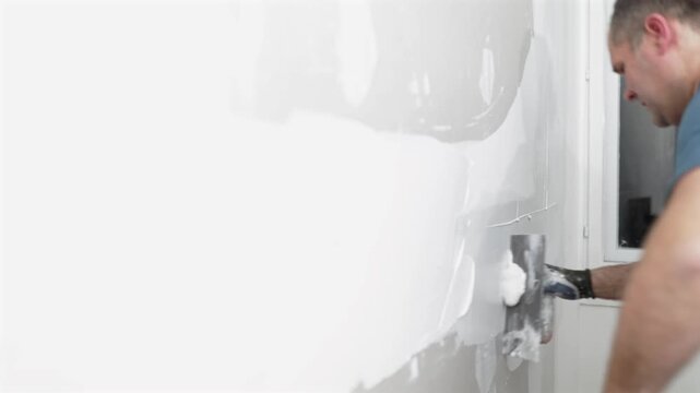 Close up video of a construction worker spreading plaster on a drywall seam with a trowel while finishing an interior wall during renovation.