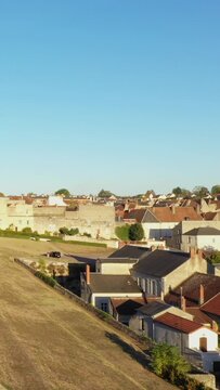 A scenic view of traditional stone houses and rooftops in La Charite sur Loire, France, under a clear blue sky. The warm sunlight highlights the charming architecture of this historic town.