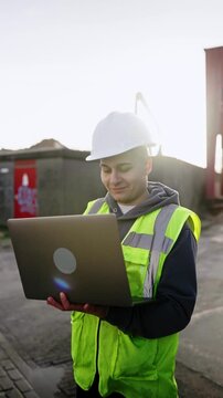 Young engineering intern working on a laptop at a construction site with a confident smile and wearing a hard hat