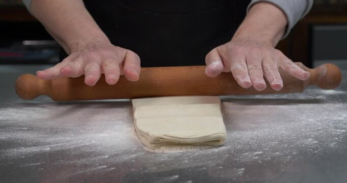 Baker Rolling Puff Pastry Dough with Wooden Rolling Pin Close Up