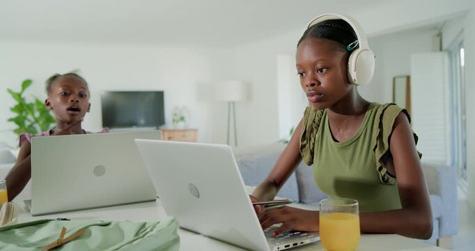 African American sisters with laptops studying at home, teen sister typing, child noticing, leaning